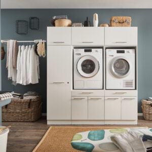 Zweigeräte Wascheinheit Ein Waschraum mit Waschmaschine und Trockner im weißen Möbelmodul, Kleiderstange mit Hemden, Körben und einem Wandwaschtrog.