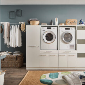 Modernes Waschkonzept Ein Waschraum mit Waschmaschine und Trockner im weißen Möbelmodul, Kleiderstange mit Hemden, offenen Regalfächern, Körben und einem Wandwaschtrog.