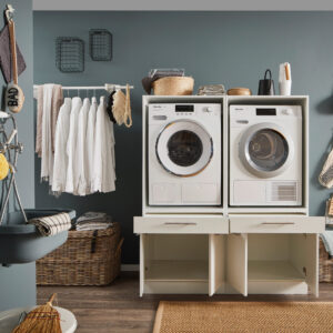 Laundreezy LDSK2W Milieu offen_91-211-17_70-200-17 Weiße Doppelstation für Waschmaschine und Trockner in einem Haushaltsraum mit geöffneten unteren Fächern.