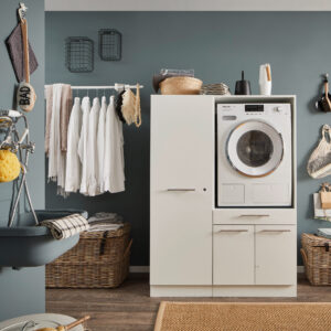 Ein moderner Waschraum mit eingebauter Waschmaschine im weißen Möbelmodul, Kleiderstange mit Hemden, Körben und einem Wandwaschtrog.