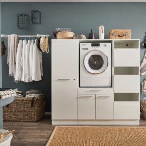 Ein heller Waschraum mit eingebauter Waschmaschine, offenen Stauraumfächern, Kleiderstange mit weißen Hemden, Körben und einem Wandwaschtrog.