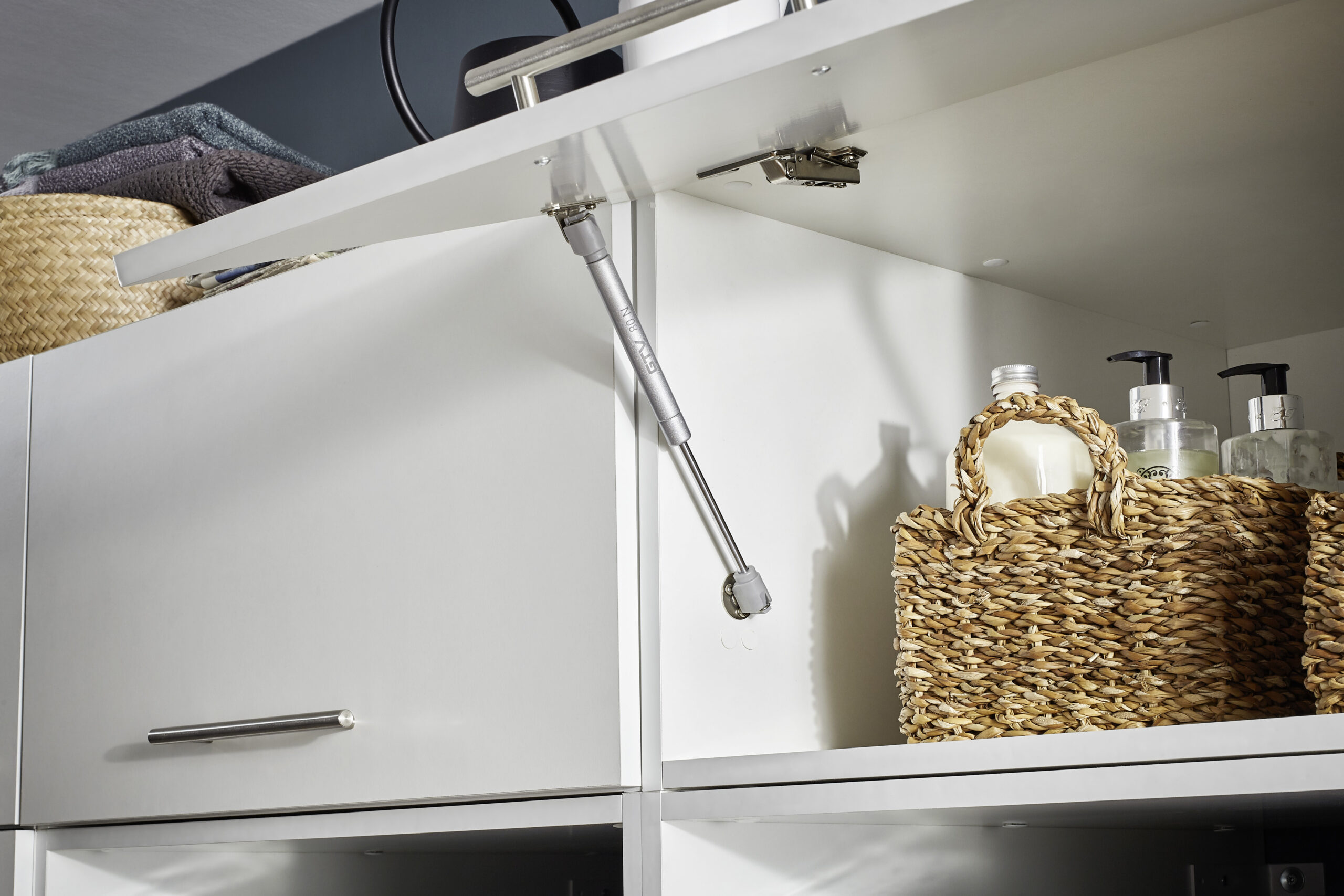 Geöffneter weißer Hängeschrank mit integriertem Liftbeschlag und gedämpfter Klappenmechanik.